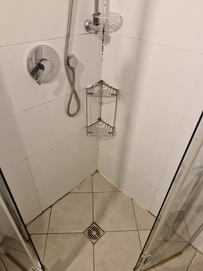 אותו מקלחון לפני העבודה: סיליקון שחור ומעופש בפינות ובמפגש קיר-רצפה